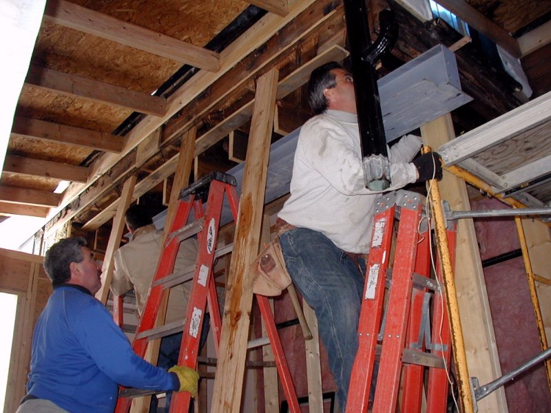 One of two supporting 'I' beams is lifted into position. Roof to left is temporary shelter