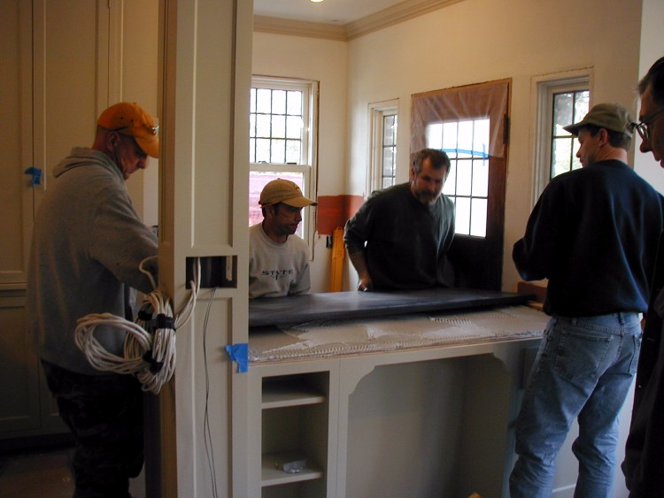Fred Peters and Matt Boucha slide granite countertop into place. Assisting are Matt's helper, left, and Kelsey, right